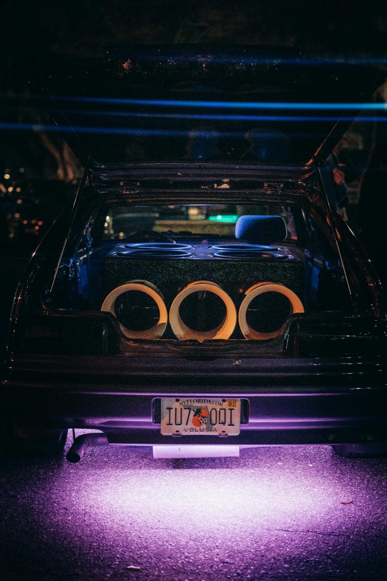 A modified car trunk featuring a powerful sound system with neon underglow lighting at night.