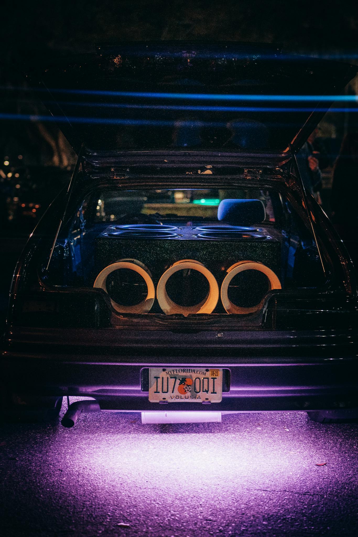 A modified car trunk featuring a powerful sound system with neon underglow lighting at night.