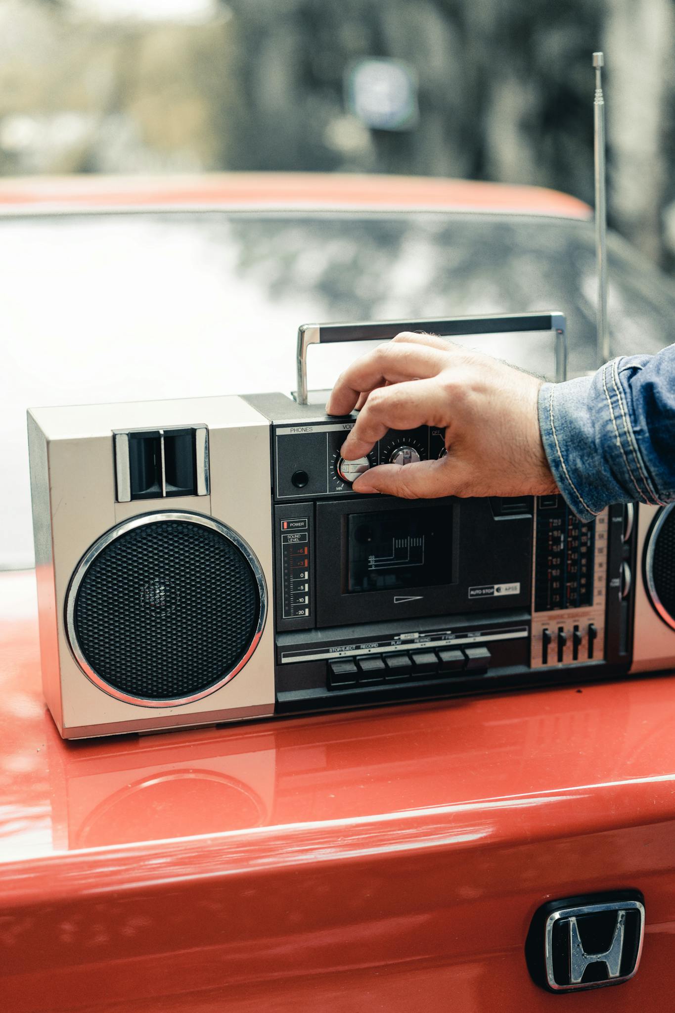 Crop anonymous male turning switch on portable boombox placed on red car trunk
