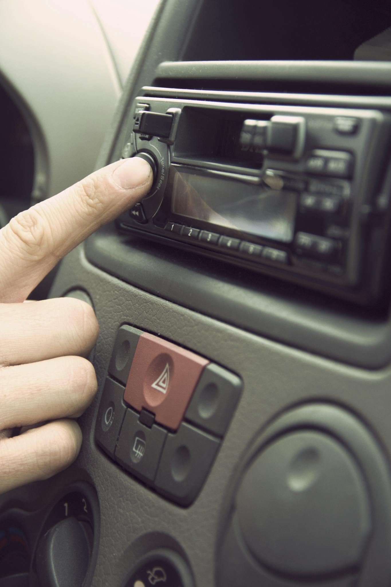 Finger adjusting car stereo in a vehicle's dashboard, depicting modern technology and music.